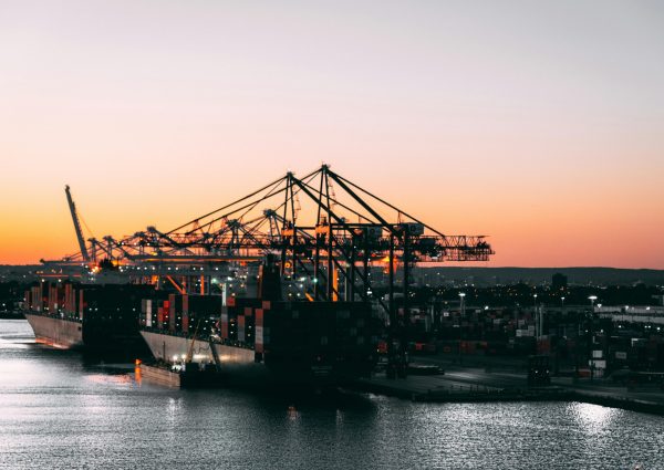 A serene view of cargo ships and cranes at a harbor during sunset, highlighting maritime industry.